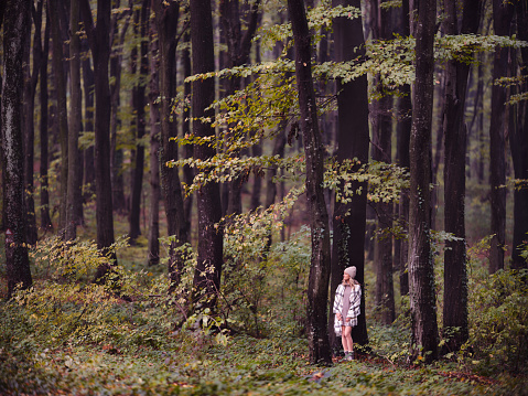 Full length of smiling woman standing among trees in autumn day at the forest. Copy space.