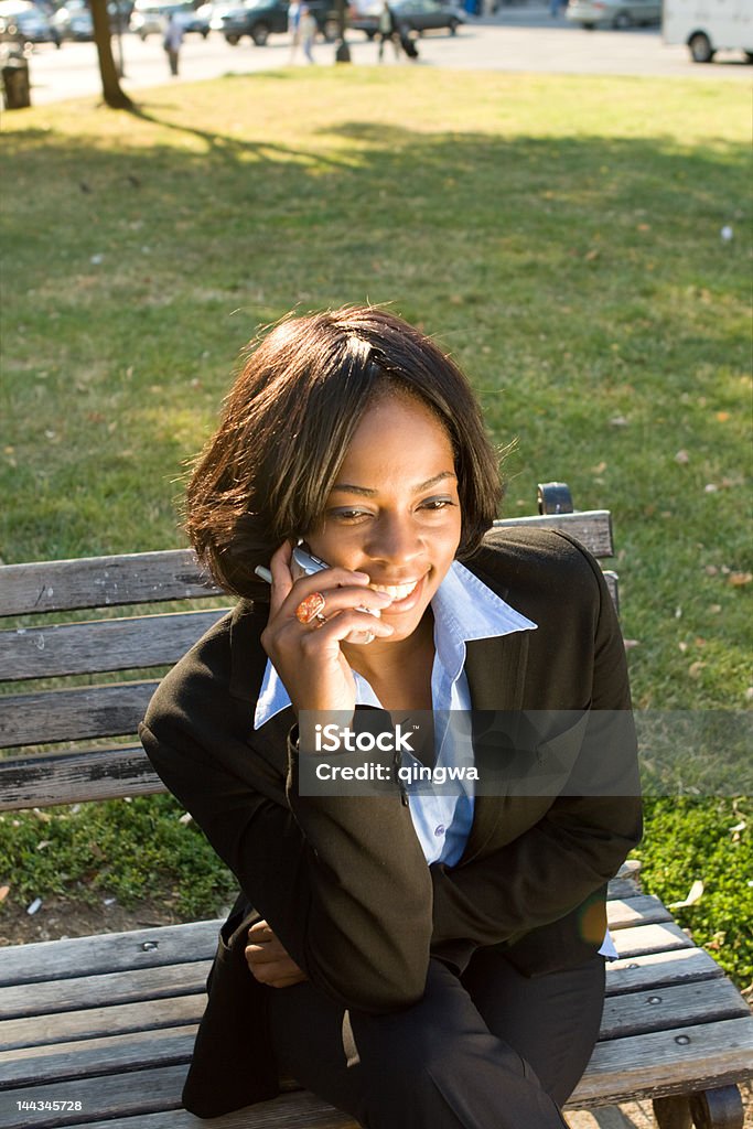 笑顔のアフリカ系アメリカ人の女性の携帯電話の公園のベンチに座る - 1人のロイヤリティフリーストックフォト