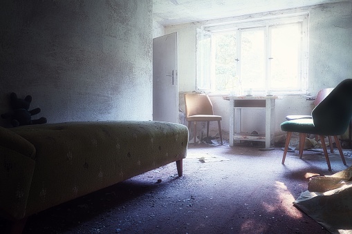 The interior of a bedroom of an abandoned house with sunlight hitting from the broken windows