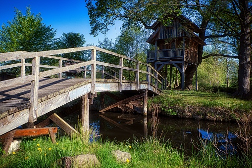 The wooden bridge above the river with a small wooden cottage on the shore.