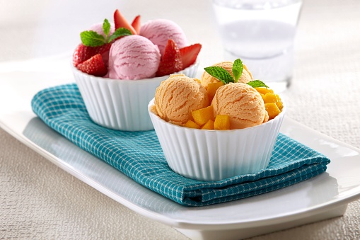 Two bowls of ice cream with strawberry and mango flavors served with pieces of fruit