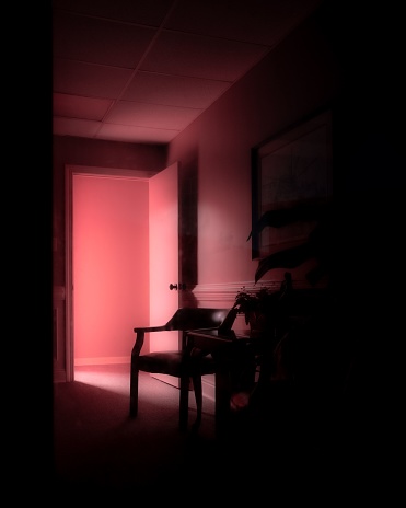 A vertical shot of a dark room interior with pink lighting coming from the open door