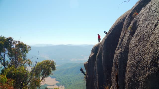 Group of mountaineers rappelling on a cliff in Australia during a bright sunny day in 4K