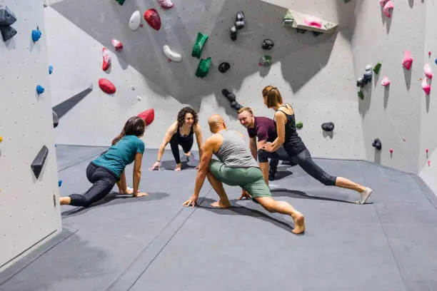 Group of rock climbers warming up before indoor climbing session. Indoor climbers stretching and preparing to climb a wall.