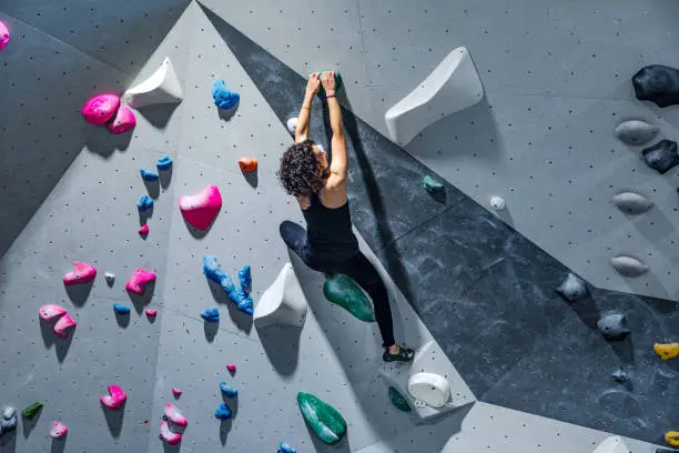 Woman in safety equipment and harness training on the artificial climbing wall. Female climbing at a indoors climbing gym.