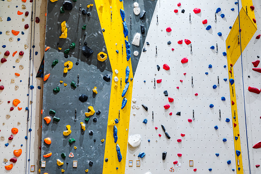 Artificial climbing walls with multi-coloured holds spread throughout the wall. Indoor rock climbing walls.