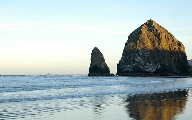 Haystack Rock at Cannon Beach Sunrise at Cannon Beach looking at Haystack Rock. The Pacific Ocean coats the beach with its calming waters creating a mirror of this rocky monolith. ocean beach papua new guinea stock pictures, royalty-free photos & images