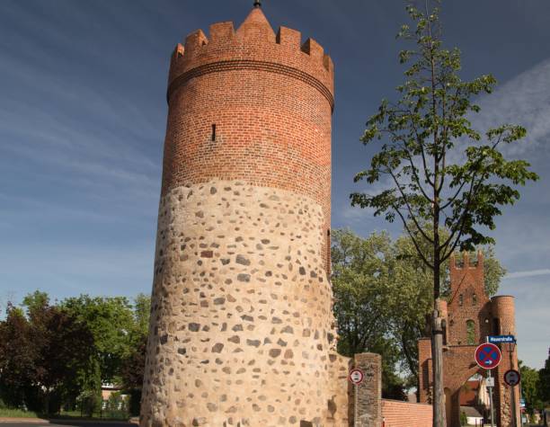 istock Round brick tower under blue cloudy sky with green trees 1443466243