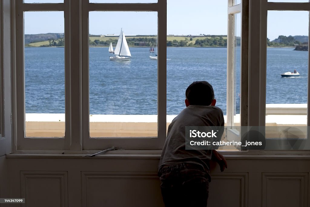 Watching Boy in silhouette looks out over Cobh harbour, Ireland Boys Stock Photo