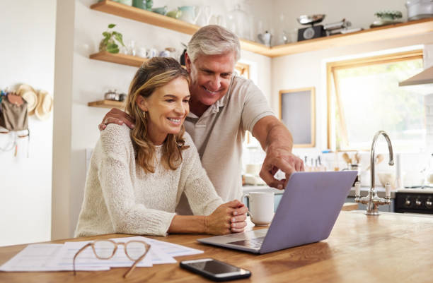 退職計画、オンラインeコマースwebサイト、またはデジタル銀行アプリケーションへの投資のためのラップトップと書類を持つ幸せな年金夫婦。高齢者、生命保険や資産運用のための高齢者 - mature adult adult couple 50s ストックフォトと画像