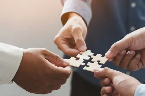 Photo of business people team holds in hand a jigsaw or puzzle pieces  in the office for concept of troubleshooting, teamwork, Unity and partnership. success and strategy concept.