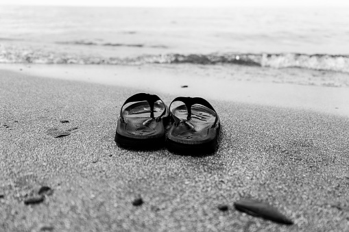 A closeup grayscale shot of slippers on the beach