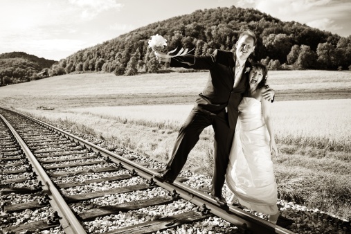 Bridal couple on rails, being in the nature. Great azure sky. Great summer! He balances with one foot on the rail. Monochrome, toned image. Looks like an old picture.