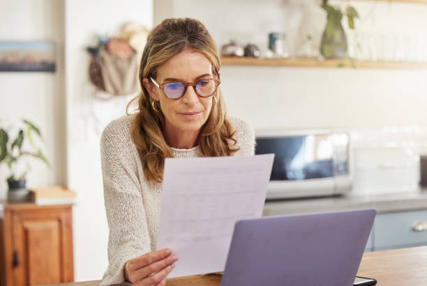 budget, finance and retirement woman with laptop and paperwork for pension savings, bills or income investment on digital bank app. elderly person with mortgage, financial document or tax management - capital letter imagens e fotografias de stock