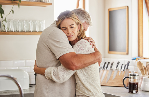 Couple, elderly and hug in kitchen in home together, romance and love. Care, man and woman in retirement love, marriage and embrace in sad moment for support, comfort and unity as married people