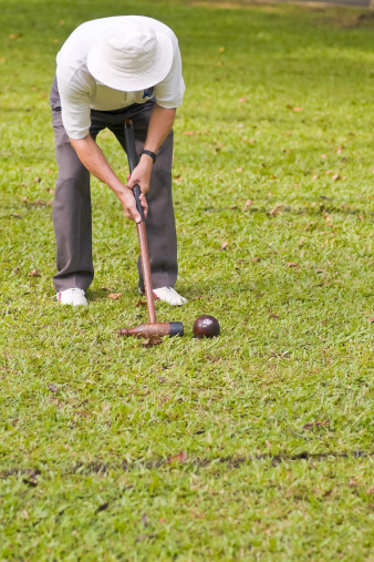 An elderly Asian man playing a variant of golf croquet in a public park, as part of a therapeutic program for people recovering from stroke/heart attack. 
