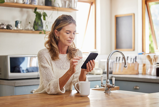 Senior woman reading phone news, mobile apps and social media notification in morning home kitchen. Relax retirement lady typing smartphone, online network website and 5g tech connection in apartment
