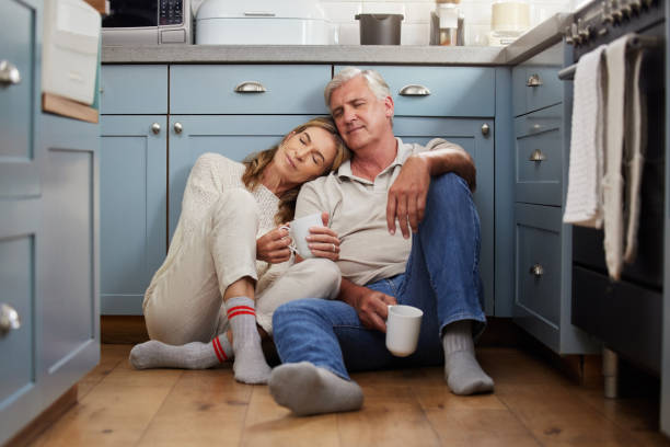 istock Senior couple, love and support while sitting together feeling safe, relax and calm drinking coffee and bonding comfortable on a kitchen floor. Happy old man and woman enjoying retirement together 1443477747