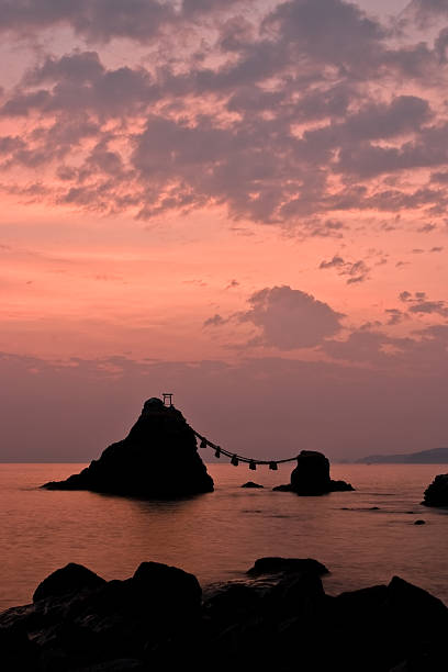 Sunrise upon  Meoto Iwa "Wedded Rocks" The ""Wedded Rocks"", are two sacred rocks in the ocean near Futami, a small town along the coast of Ise City (Mie, Japan).  In Shinto belief, the rocks represent the union of creator gods Izanagi and Izanami. Thus celebrating the union in marriage of man and woman. The shimenawa rope connecting the two weighs over a ton. The larger rock, said to be male, has a small tori at its peak. mie prefecture photos stock pictures, royalty-free photos & images