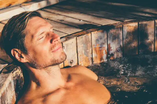 Photo of Man relaxing in wooden hot tub outdoor.