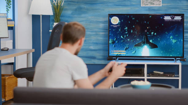 istock Man holding wireless controller playing console video game first person shooter on tv while sitting on sofa 1443482993