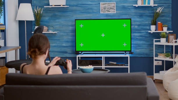 istock Gamer girl playing console video games with wireless controller on green screen tv relaxing on couch 1443483113