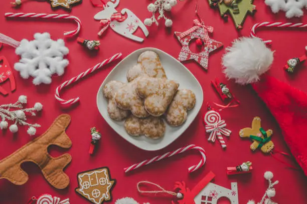 Christmas table flat lay composition. Delicious heart-shaped gingerbread cookies, candy canes, Santa Claus hat and Christmas Tree decorations, decor pendant ornaments.