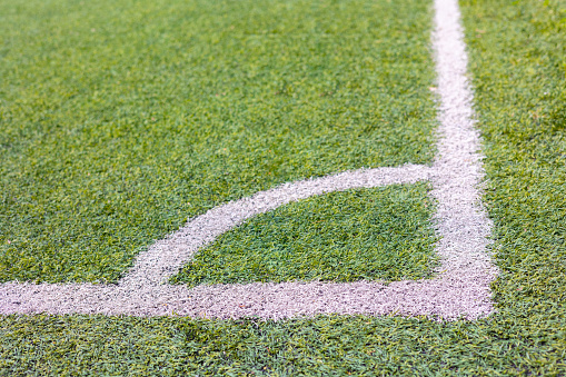 Close up shot of white line of chalk for corner symbol on lawn or grass in soccer field under sunlight in summer shows concept of sport and leisure time activities outdoor for competition.