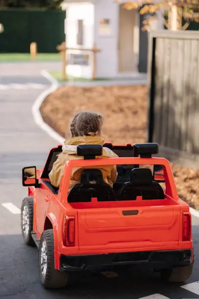 Cute little girl rides in a mini city on a red electric car jeep. Adorable little girl road in toy city. Plays for entertaiment.
