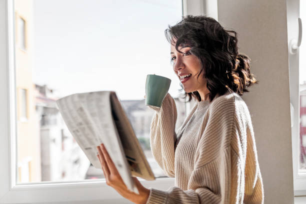 istock Woman drinking cup of coffee while reading newspaper at home 1443493536