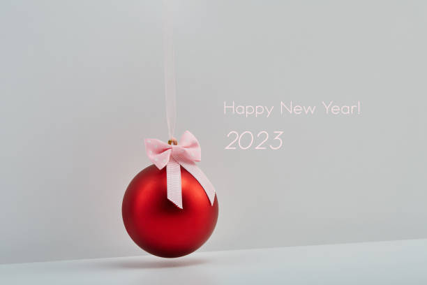 빨간 크리스마스 공은 2023년 새해 복 많이 받으세요 텍스트가 있는 흰색 배경 위에 활과 함께 리본에 매달려 있습니다. 휴일과 새해 개념 - love hanging indoors studio shot 뉴스 사진 이미지