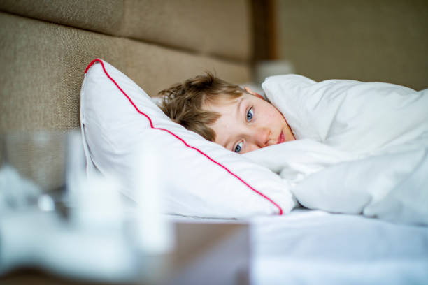 School age boy laying in bed with a flu stock photo