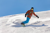 Young adult man snowboarding in mountains at ski resort