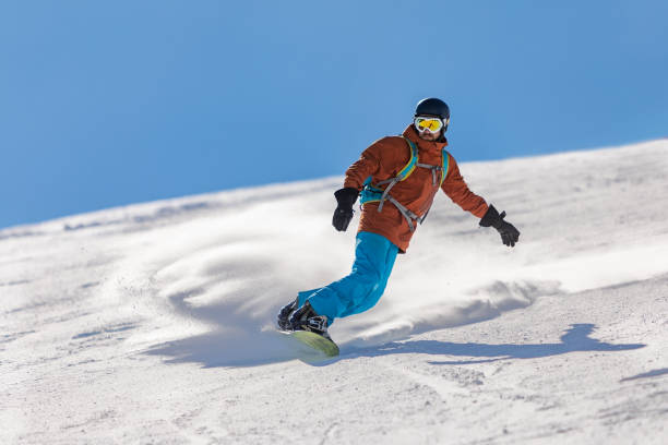 Young adult man snowboarding in mountains at ski resort stock photo