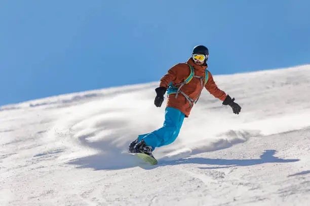 Young adult man snowboarding in mountains at ski resort