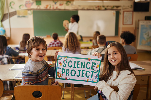 Happy elementary students holding a placard during a science class at school and looking at camera.