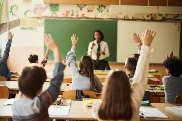 istock Back view of students raising their hands to answer the teacher's question on a class. 1443498002