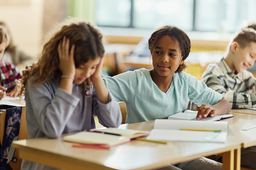 African American schoolgirl consoling her displeased friend on a class at elementary school.