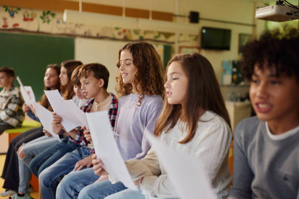 School kids practicing with sheet music on a class at school. Large group of elementary students singing on a music class at school. Focus is on happy girl. school choir stock pictures, royalty-free photos & images