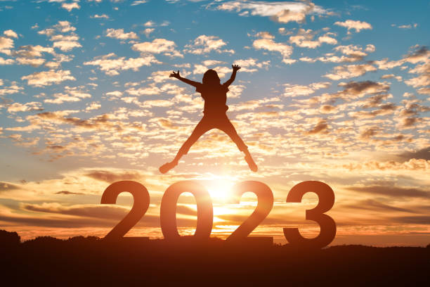 Silhouette of young woman jumping to Happy new year 2023 in sunset or sunrise background. stock photo