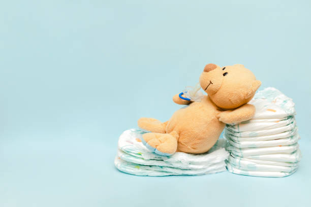istock Stack of diapers with cute teddy bear toy pacifier lying on table. set for infant newborn boy girl for baby shower present gift on blue background with copy space. Healthcare medical, hygiene concept 1443500186