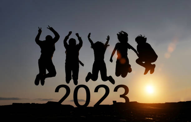 Happy group of people celebrate jump for new year 2023. concept for win victory. silhouette of friends jumps at sunset time on mountains. stock photo