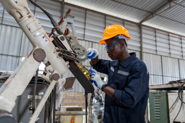 afroamerikanischer fabrikingenieur, der mit einem geschickten roboterarm in der werkstatt arbeitet. männlicher ingenieur wartung automatische roboterarmmaschinen in der fabrik. fertigungstechnologie für industrieroboter - cnc vehicle part quality control industry stock-fotos und bilder