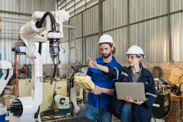 gruppo di ingegneri maschi e femmine che utilizzano il controller del robot che lavora con un braccio robotico esperto in officina. team di tecnici che lavorano con il sistema di saldatura automatica del braccio robotizzato di controllo in fabbrica - cnc vehicle part quality control industry foto e immagini stock