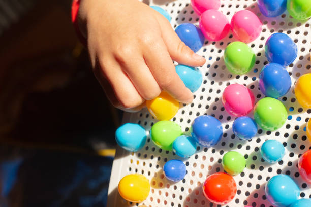 Baby plays with colourful mosaics on white surface. Kids hand with bright constructor for developing creativity and motor skills. Early education. Puzzle for preschoolers. Fingers with toy in sunlight. High quality photo el bebé juega con mosaicos de colores sobre superficie blanca. los niños tienen la mano de un constructor brillante para desarrollar la creatividad y las habilidades motoras. educación temprana. rompecabezas para niños en edad preescolar. dedos con jug