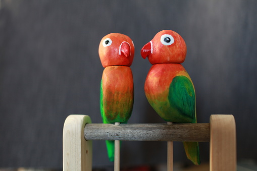 pair of red-green lovebird parrots wooden toy blurred  background