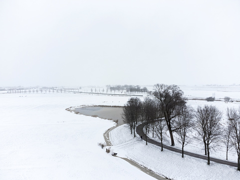 Snowy winter landscape with an old levee winding into the distance in the IJsseldelta region near Kampen in Overijssel during an overcast winter day.