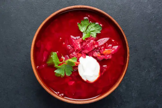 Beetroot Borscht soup with sour cream in a bowl, isolated on black concrete table. Top view
