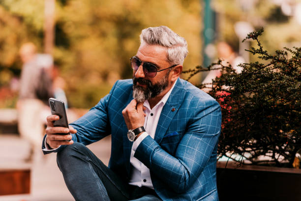 istock Modern senior businessman using smartphone for online meeting while sitting on bench 1443506001