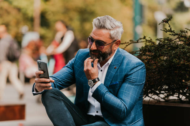 istock Modern senior businessman using smartphone for online meeting while sitting on bench 1443506010